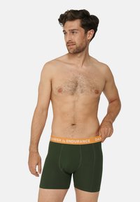 Tmavě zelené boxerky s oranžovým páskem označeným "DANISH ENDURANCE." Vyrobené z měkkého materiálu, s přiléhavým střihem.