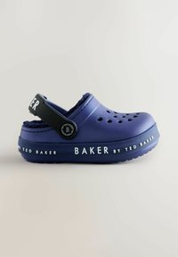 Ljubičasto klompa s crnim remenom, s ventilacijskim rupama i mekanim podstavom. Brendiranje glasi "BAKER by TED BAKER" na potplatu. Teksturirani gumeni materijal.