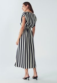 Maksimekko, jossa on musta- ja kermanvärisiä pystysuoria raitoja, lyhyet hihat, rypistetty vyötärö ja valuva kangas. Korkeat sandaalit näkyvissä.