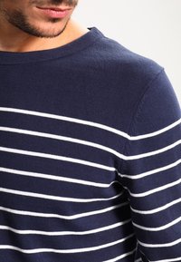 Suéter de punto azul marino con rayas blancas horizontales, cuello redondo y tejido texturizado, mostrando una vista en primer plano de la parte superior del cuerpo.