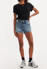 Black short-sleeve shirt paired with frayed hem, distressed denim shorts in a light blue wash, worn with gray athletic sneakers and black socks.