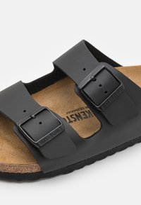 Black Birkenstock sandals featuring two adjustable straps and metal buckles, with a cork footbed and textured outsole.