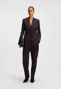Mørkeblå skræddersyet jakkesæt med en blazer med én knap og bredbenede bukser. Modellen holder en sort håndtaske og har høje støvler på.