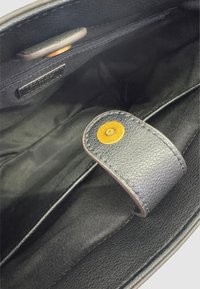 Interno di una borsa a tracolla nera in pelle con una trama liscia. Presenta un pulsante circolare giallo e una tasca con zip lungo il bordo superiore. Fodera in tessuto scuro.