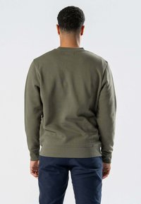 Oliven grøn bomulds sweatshirt, rund hals, ribbede manchetter og kant, glat tekstur, iført med marina blå bukser, vist fra ryggen.