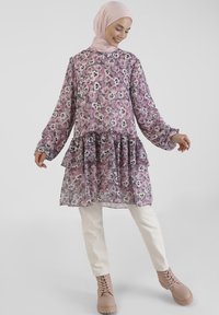 Floral tunic with long sleeves, layered ruffle hem, featuring pink, purple, and white patterns. Paired with light-colored pants and lace-up boots.