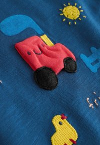 Camion en tissu rouge avec des roues noires et de la fumée bleue sur un fond bleu foncé, avec un soleil jaune et des détails brodés de poussin.