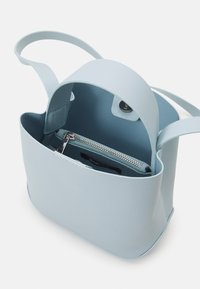 Borsa a mano azzurro chiaro con manico superiore e pattina magnetica, che mostra una tasca interna con zip e una tracolla corta.
