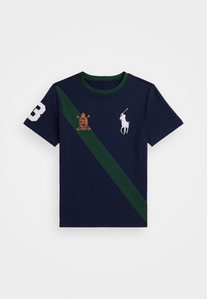 T-shirt bleu marine à manches courtes avec une bande diagonale verte, logo joueur de polo blanc, écusson brodé avec "20" et numéro blanc "3" sur la manche.
