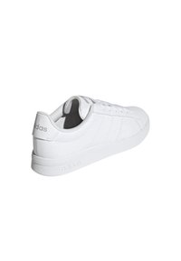 Zapatilla baja blanca de Adidas con cierre de cordones en la parte delantera, cuello acolchado y discretos logotipos de la marca en el talón y la suela, presentada en ángulo para mostrar los lados exterior y trasero.