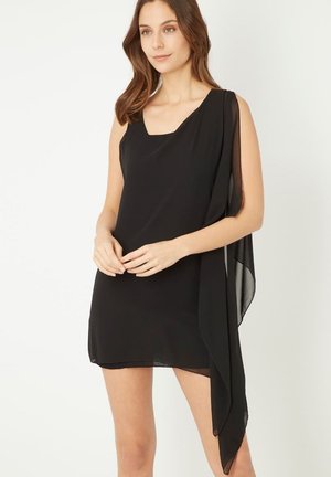 Vestido negro sin mangas con escote cuadrado y caída lateral transparente, que presenta una tela suave y fluida que aporta movimiento y elegancia.