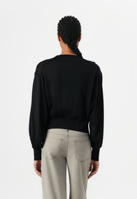 Black pullover sweater with puffed sleeves and ribbed hem, paired with light gray high-waisted trousers featuring back pockets and stitch detailing.