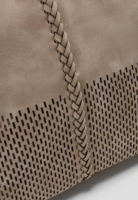 Surface en cuir taupe avec une bande de cuir tressée et un motif de découpes rectangulaires verticales en dessous.