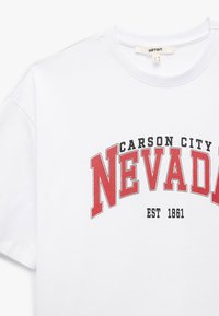 Witte katoenen t-shirt met een rood en zwart "NEVADA" graphic met gebogen tekst. Eenvoudige ronde halslijn en korte mouwen.