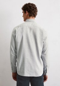 Chemise à manches longues gris clair en tissu texturé, avec un col boutonné et des poignets ajustables, dotée d'un ourlet arrondi à la taille.