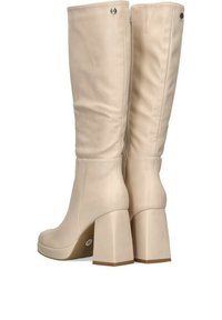 Botas de caña alta en beige, hechas de material sintético suave, con un tacón ancho, cierre de cremallera y acentos decorativos de botones.