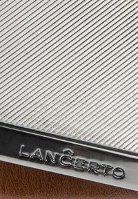 Metalowy portfel o teksturowanym srebrnym wykończeniu i ukośnych rowkach, z brązowym skórzanym spodem i wytłoczonym logo "Lancerto".