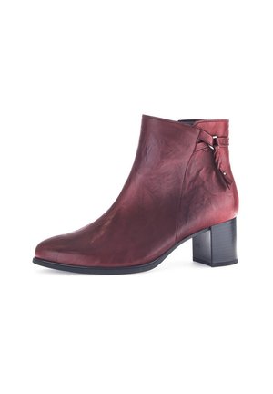 Bottine en cuir rouge avec un talon bloc, bout pointu et sangle latérale décorative avec un détail à frange. Texture lisse avec une finition brillante.