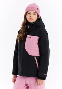 Zwarte en roze skijas met een ritszak, capuchon en versterkte manchetten. Gekoeld met roze sneeuwbroeken en een lichtroze gebreide muts.