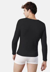 Camisa negra de manga larga hecha de tejido elástico, diseño ajustado y escote amplio, combinada con ropa interior blanca. Se muestra la vista trasera.