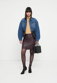 Traperica s oversized rukavima, senf žuti pulover, bordo kožna suknja, crne sandale s remenom oko gležnja i mala crna torbica s zakovicama.