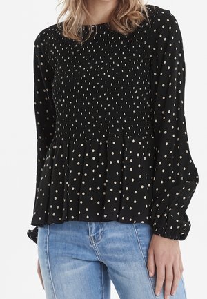 Blusa nera a maniche lunghe con corpino arricciato e orlo plissettato, caratterizzata da un motivo a pois in beige chiaro. Tessuto morbido e leggero.