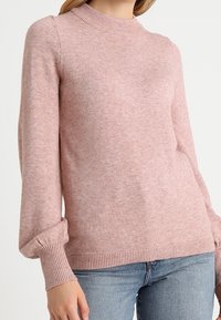 Světle růžový svetr s vysokým výstřihem, dlouhými rukávy a žebrovanými manžetami a lemem. Vyrobený z měkké, strukturované tkaniny.