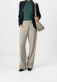 Blazer bleu marine sur un top vert ajusté, pantalon beige à jambes larges avec taille élastique et sac à bandoulière marron clair. Chaussures plates noires.