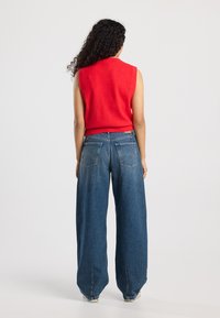 Red sleeveless top paired with wide-leg blue denim jeans. The fabric appears soft, and the design features a fitted waist and a relaxed fit.