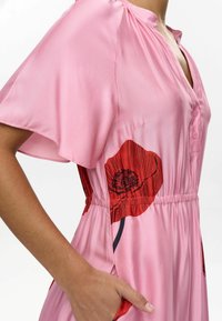 Pink satin dress with short sleeves, featuring a red poppy print, a buttoned collar, and an elastic waistband. Includes side pockets.