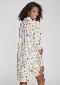 Långärmad klänning i lätt tyg med blommönster i gult och blått på vit bakgrund, med en lös passform och krage med knappar.
