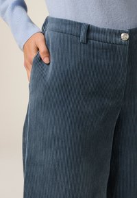 Dunkelblaue Baumwollcordhosen mit vertikalen Rippungen, ausgestattet mit einem Gürtelschlaufen und einer Vordertasche, sowie einem silbernen Knopfakzent.