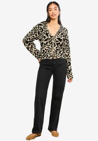 Pletený cardigan v béžové barvě s černým leopardím potiskem, má výstřih do V, přední knoflíky a dlouhé rukávy, doplněný černými kalhotami a béžovými botami.