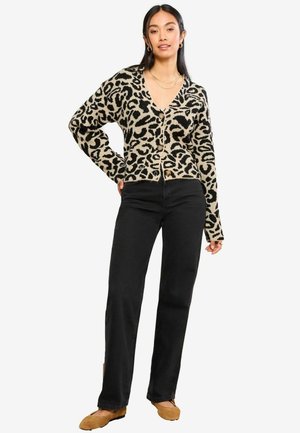 Cardigan tricotat în bej cu imprimeu leopard negru, având decolteu în V, nasturi frontali și mâneci lungi, asortat cu pantaloni negri și pantofi bej.