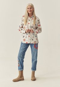 Valge lillemustriga särk, sinised tikitud teksad ja beež pahkluu saapad. Iseloomustab värvikate mustrite ja tekstuuride segu.