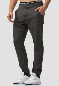 Pantalones tapered de color gris oscuro con una textura suave, que presentan bolsillos laterales y detalles de costura. Combinados con zapatillas blancas para crear contraste.