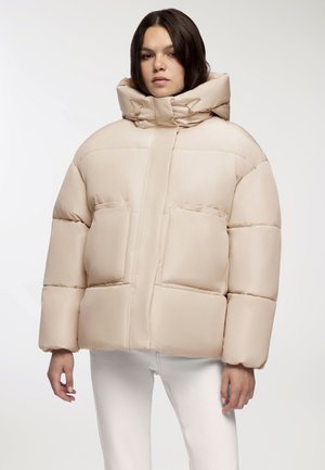 Giacca a vento beige con cappuccio oversize, trapuntatura orizzontale, due tasche frontali e una superficie liscia e lucida.