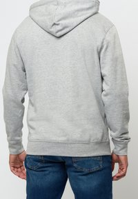 Felpa grigia con cappuccio in materiale morbido e coulisse. Presenta polsini e orlo a coste, abbinata a jeans di denim blu.