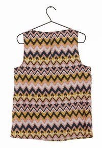 Débardeur sans manches avec un motif en zigzag noir, rose, jaune et blanc. Fabriqué en tissu texturé, il dispose d'une fermeture à boutons à l'arrière. Accroché à un crochet noir.