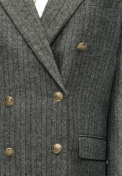 Dvigubas pilkas švarkas su herringbone raštu, šešiais auksiniais kaukolių rašto sagomis, įpjovomis apykaklėmis ir kišene detailė.