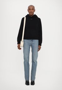 Svart hettegenser med kengurulomme, lyseblå rettbente jeans, sorte ankelstøvler og liten kremfarget crossover-veske.