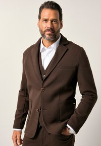 Blazer marrone realizzato in tessuto textured con due bottoni, revers a scollo a V e tasche laterali; indossato sopra una camicia bianca e un gilet coordinato.