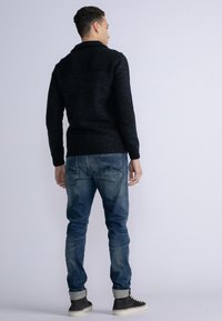 Pulover negru din tricot cu guler ribbed și petice la coate, combinat cu blugi decolorati și adidași gri, văzut din spate.