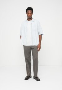 Μπλε πουκάμισο με ανοιχτές ρίγες και κοντά μανίκια πάνω από ένα λευκό μπλουζάκι, συνδυασμένο με γκρι παντελόνι και μαύρα παπούτσια. Το πουκάμισο έχει τσέπη στην αριστερή πλευρά.