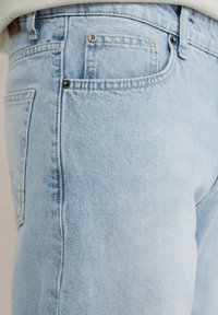 Lichtblauwe denim jeans met een vervaagde textuur, voorzien van een voorzak en een metalen knoopsluiting, ontworpen voor een standaard pasvorm.