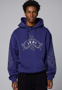 Marine hoodie met witte "ARMY" tekst en decoratieve vlamachtige borduursels op de mouwen. Zacht materiaal, oversized ontwerp, kangoeroezak.