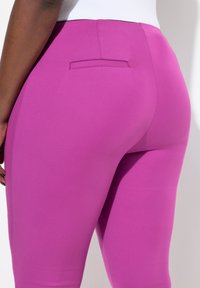 Leggings aderenti in tessuto rosa vivace, caratterizzati da una superficie liscia e un dettaglio con tasca posteriore. La vita è elegante ed elastica.
