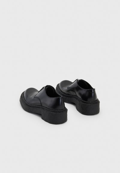 Black leather shoes with a rounded toe and thick, textured black rubber soles. Features minimal stitching and a smooth finish.