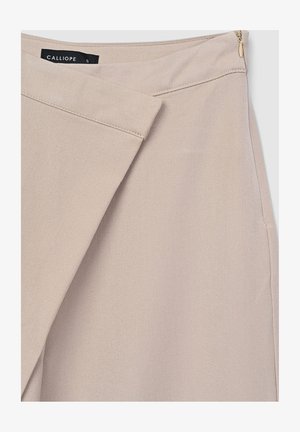 Jupe asymétrique beige avec un panneau avant superposé, fermeture éclair sur le côté et étiquette de marque noire visible "CALLIOPE" en taille petite.
