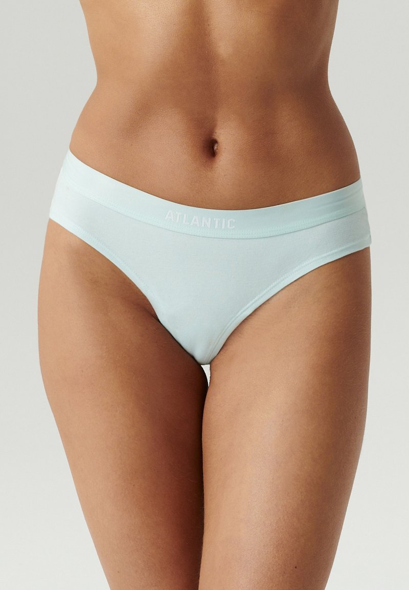 Kobieta nosząca jasnoniebieskie bawełniane majtki z logo "ATLANTIC" na pasku, pokazana od talii do górnej części ud na neutralnym tle.